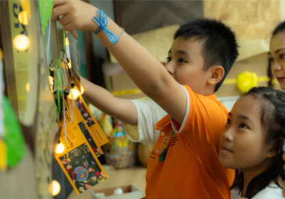 Two children hang a craft piece on a decorated wall. 