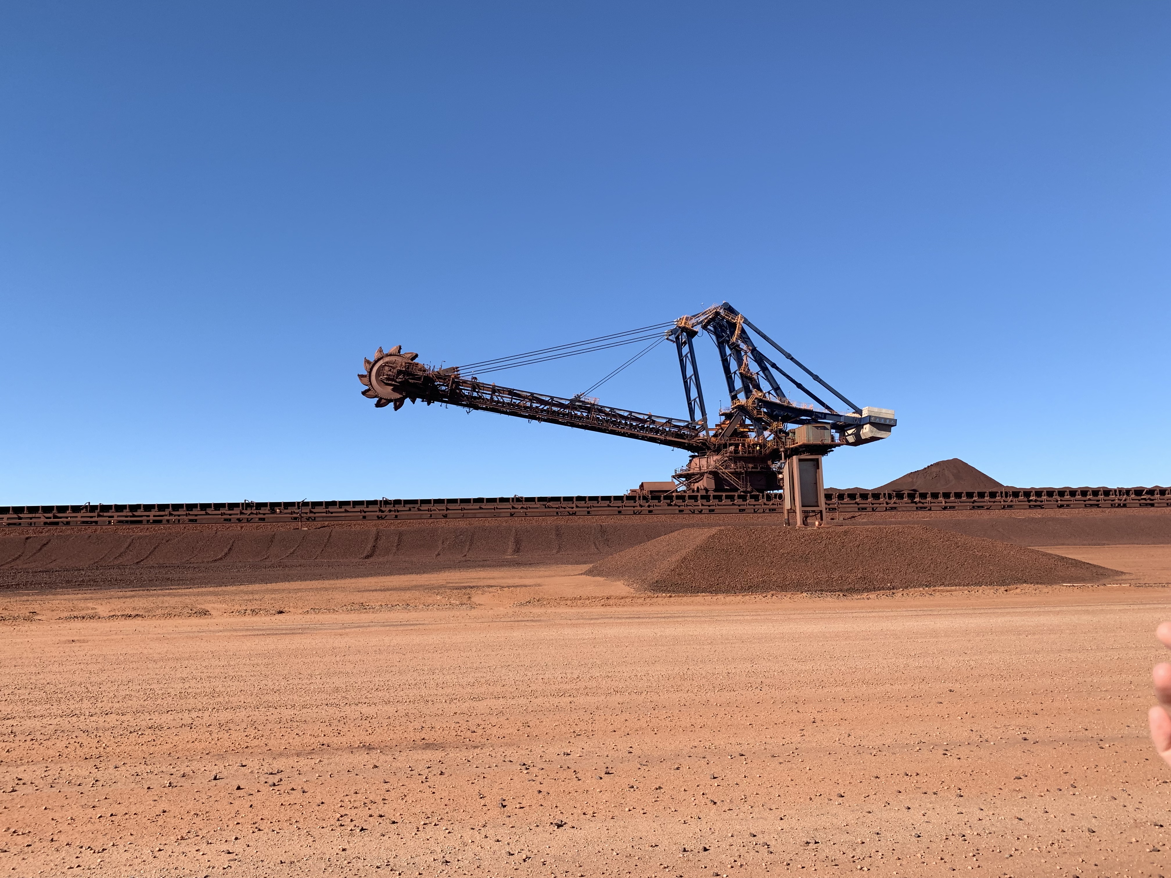 Bucket wheel reclaimer operating at an iron ore stockyard under a clear blue sky in Western Australia.